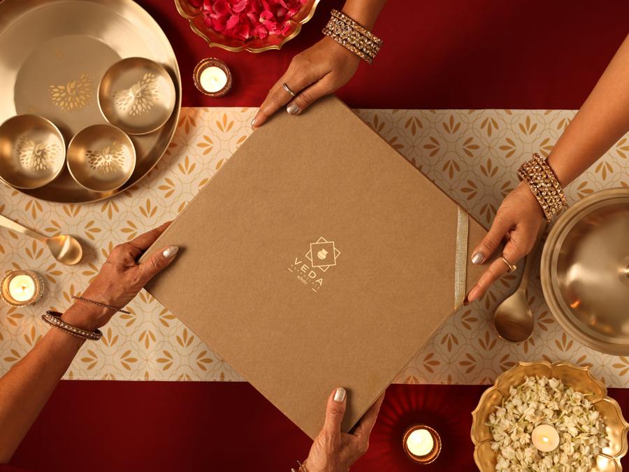 Hands passing a Veda gift box across a festive table
